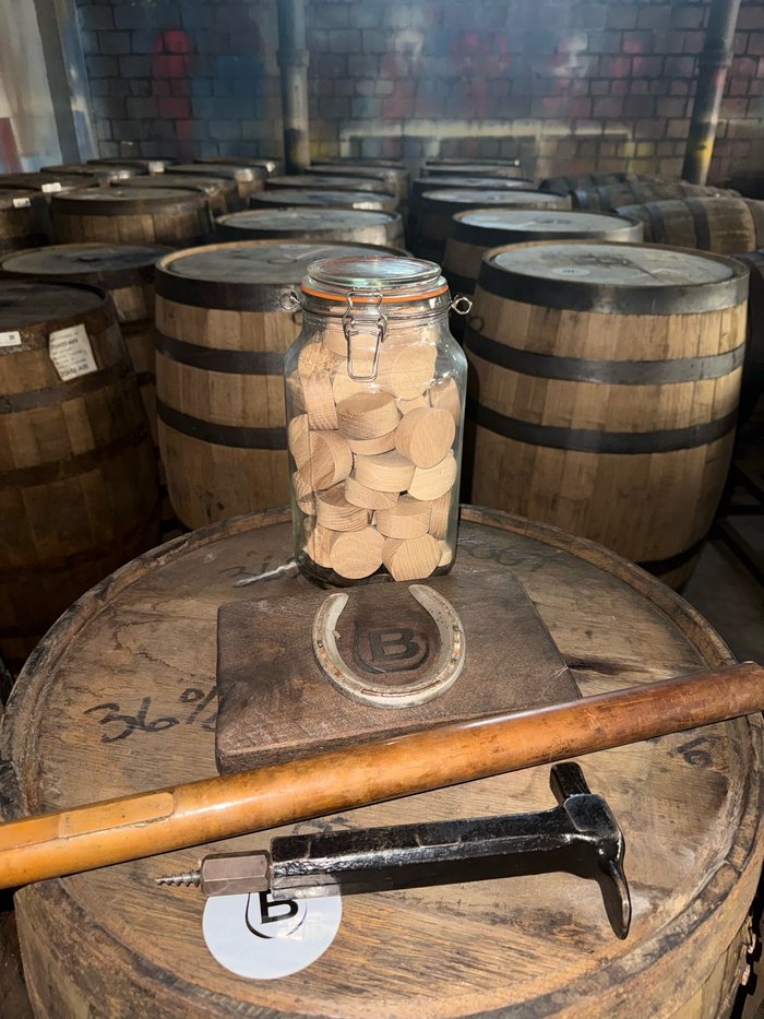A whiskey thief and jar on a horseshoe in front of rows of barrels